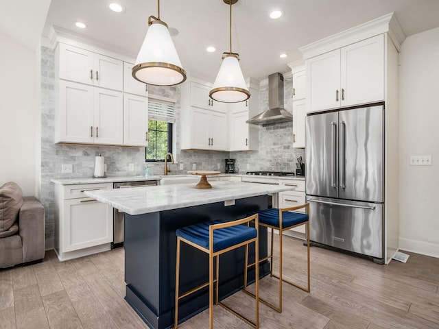 kitchen with hanging light fixtures, wall chimney exhaust hood, appliances with stainless steel finishes, light hardwood / wood-style floors, and white cabinetry