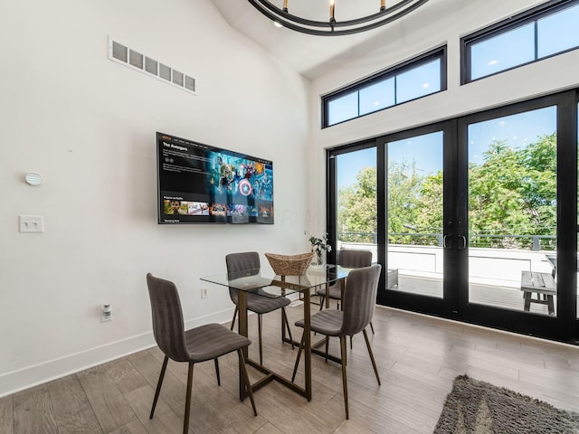 dining space with french doors, an inviting chandelier, a high ceiling, and hardwood / wood-style flooring