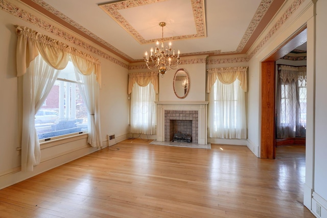 unfurnished living room with ornamental molding, a tiled fireplace, a tray ceiling, plenty of natural light, and light wood finished floors