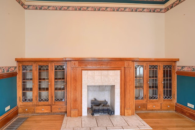 interior space featuring a tiled fireplace, visible vents, baseboards, and wood finished floors