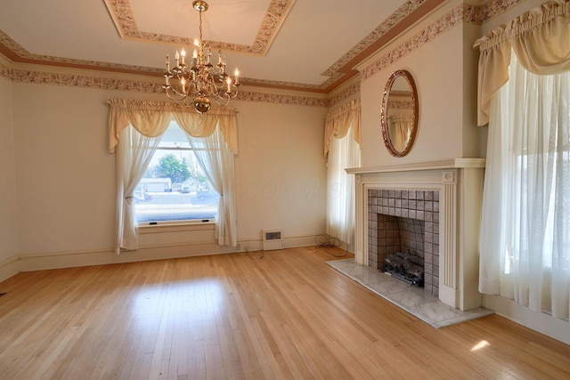 unfurnished living room featuring a raised ceiling, a tiled fireplace, hardwood / wood-style floors, an inviting chandelier, and baseboards