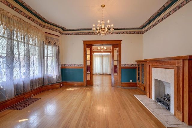 unfurnished living room featuring visible vents, a tile fireplace, light wood-style floors, crown molding, and a chandelier