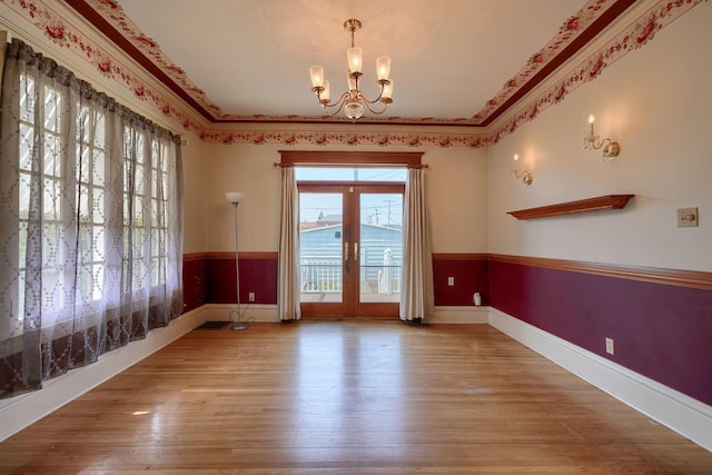 empty room featuring a notable chandelier, wainscoting, crown molding, and wood finished floors