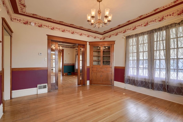 empty room with baseboards, a notable chandelier, crown molding, and light wood finished floors