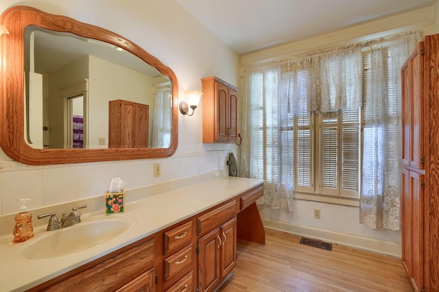 bathroom with vanity, wood finished floors, visible vents, baseboards, and decorative backsplash