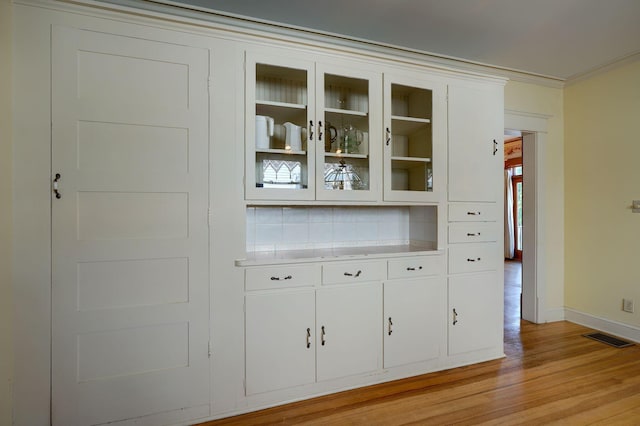 interior space with visible vents, baseboards, crown molding, light wood-type flooring, and backsplash