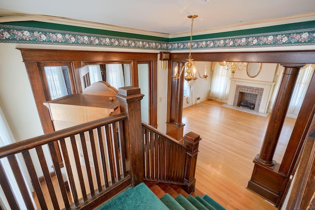 stairway featuring a tiled fireplace, a notable chandelier, ornamental molding, and wood finished floors