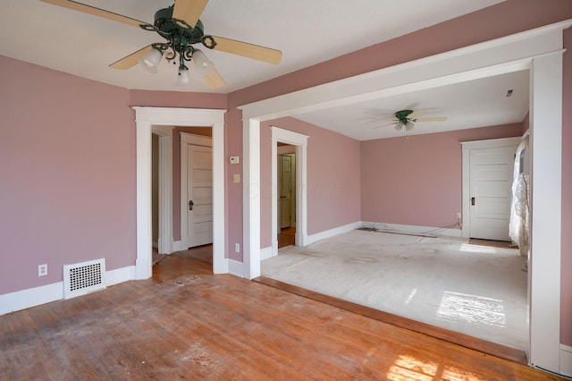 empty room with a ceiling fan, wood finished floors, visible vents, and baseboards