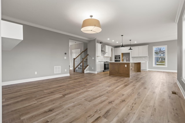 unfurnished living room featuring light hardwood / wood-style floors, crown molding, and sink