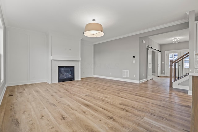 unfurnished living room with a barn door, light hardwood / wood-style flooring, and crown molding