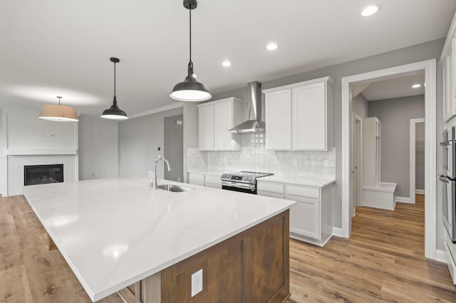 kitchen with a spacious island, wall chimney range hood, sink, electric stove, and white cabinetry