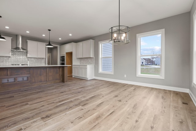 kitchen featuring wall chimney range hood, tasteful backsplash, pendant lighting, light hardwood / wood-style floors, and white cabinets