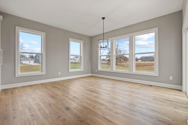 unfurnished dining area with plenty of natural light, an inviting chandelier, and light wood-type flooring