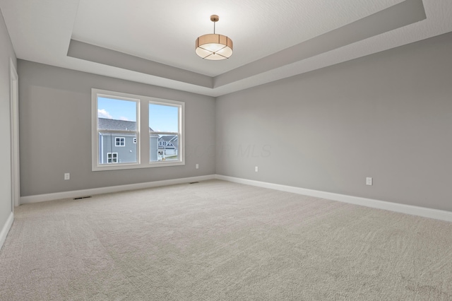 carpeted empty room with a raised ceiling