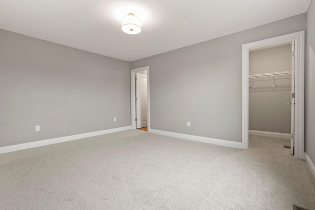 unfurnished bedroom with a walk in closet, a closet, and light colored carpet