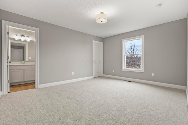 unfurnished bedroom with connected bathroom, sink, and light colored carpet