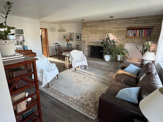 living room featuring a chandelier, a stone fireplace, crown molding, and dark wood-type flooring