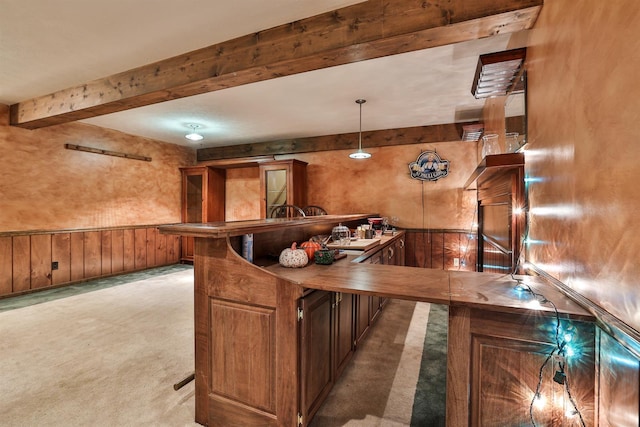 kitchen featuring pendant lighting, a breakfast bar, wood walls, light carpet, and beamed ceiling