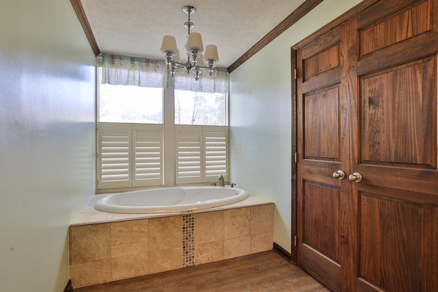 bathroom featuring hardwood / wood-style floors, ornamental molding, a textured ceiling, tiled bath, and a chandelier