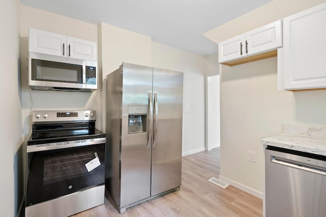 kitchen featuring appliances with stainless steel finishes, light wood-type flooring, white cabinetry, and light stone counters