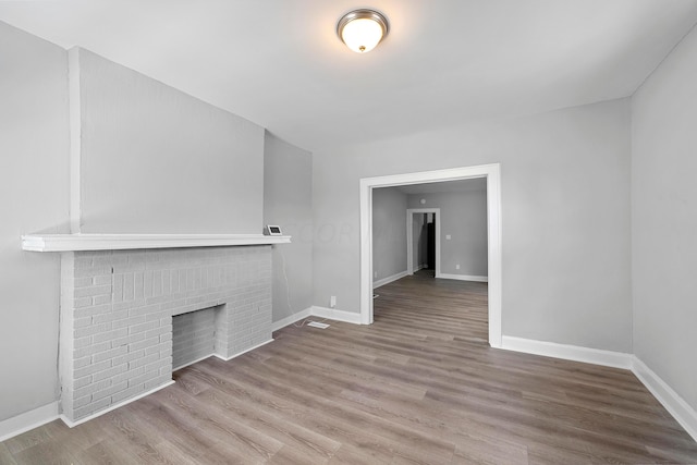 unfurnished living room featuring hardwood / wood-style flooring and a brick fireplace