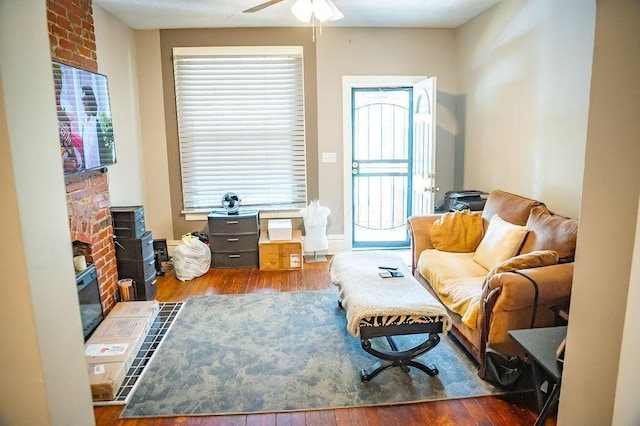 sitting room featuring ceiling fan, dark hardwood / wood-style floors, and a brick fireplace