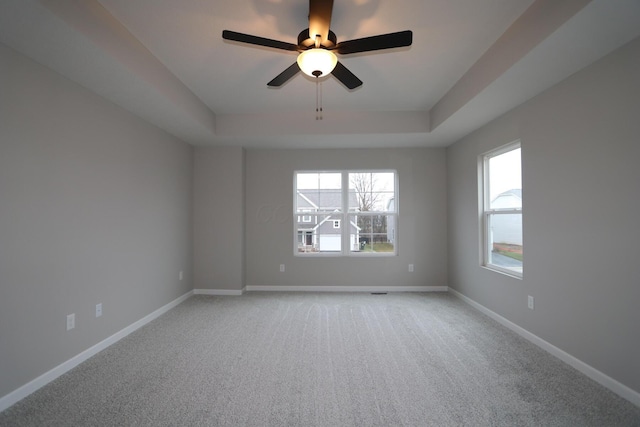 carpeted spare room with a raised ceiling and ceiling fan