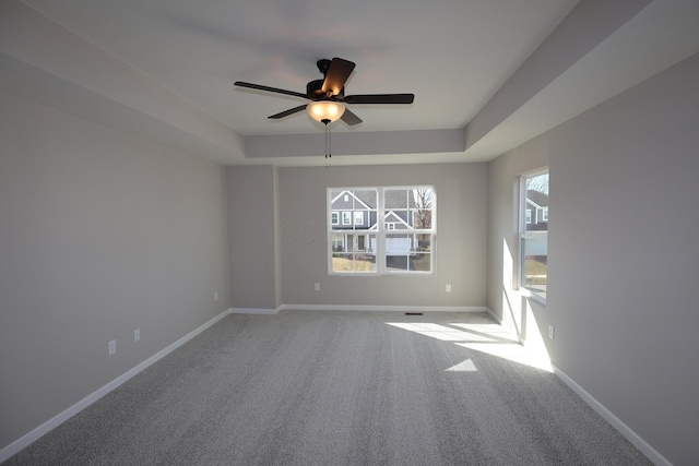 carpeted empty room featuring a tray ceiling, a ceiling fan, and baseboards