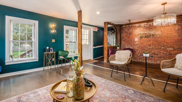 sitting room with an inviting chandelier, dark wood-type flooring, and brick wall