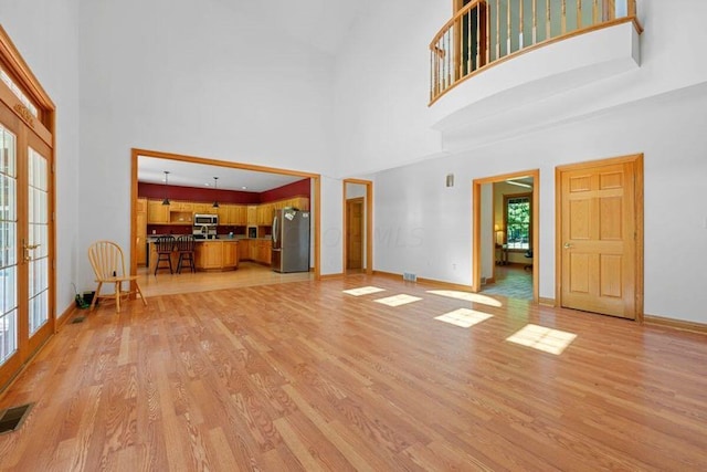 unfurnished living room with a high ceiling, light wood-type flooring, and french doors