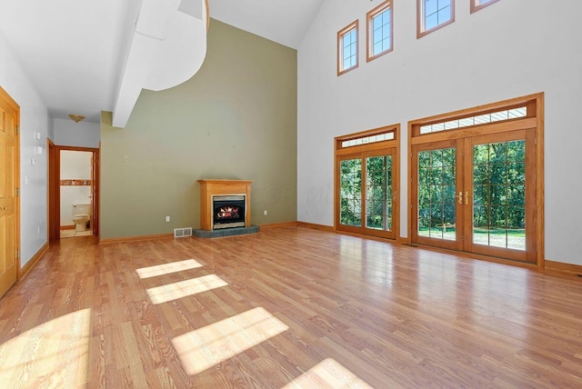 unfurnished living room featuring light wood-style flooring, a healthy amount of sunlight, a lit fireplace, and baseboards