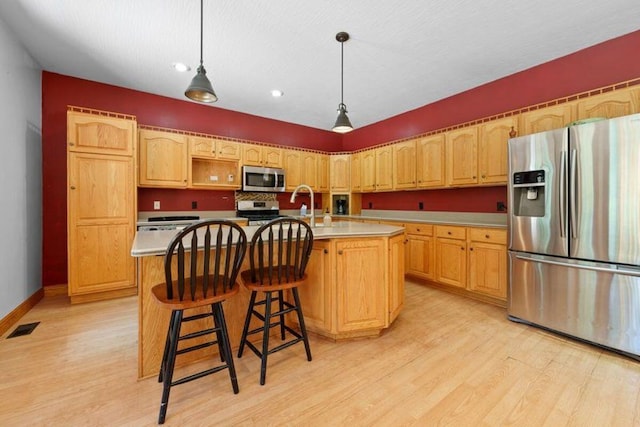 kitchen with hanging light fixtures, light wood-type flooring, a kitchen island with sink, and appliances with stainless steel finishes