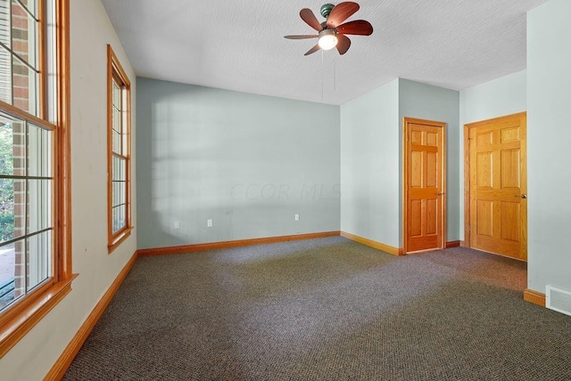 empty room with a textured ceiling, dark colored carpet, a ceiling fan, and baseboards