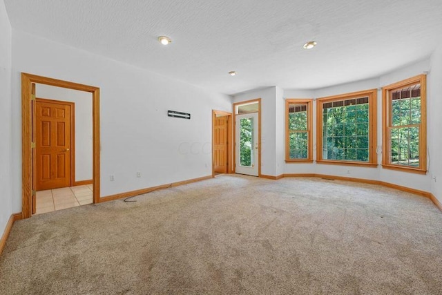 spare room with light carpet, baseboards, and a textured ceiling