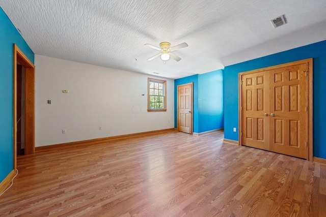 unfurnished bedroom featuring a textured ceiling, a ceiling fan, baseboards, visible vents, and light wood-style floors