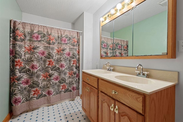 full bath with a textured ceiling, double vanity, a sink, and visible vents