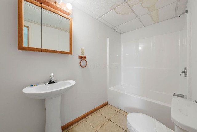 bathroom featuring a paneled ceiling, toilet, baseboards, shower / washtub combination, and tile patterned floors