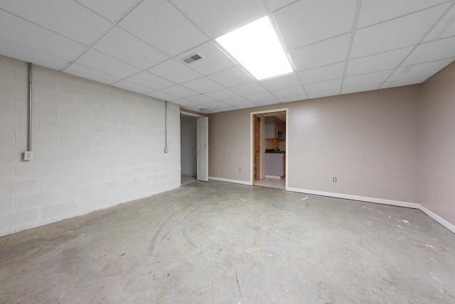 finished basement featuring visible vents, a drop ceiling, concrete block wall, and baseboards