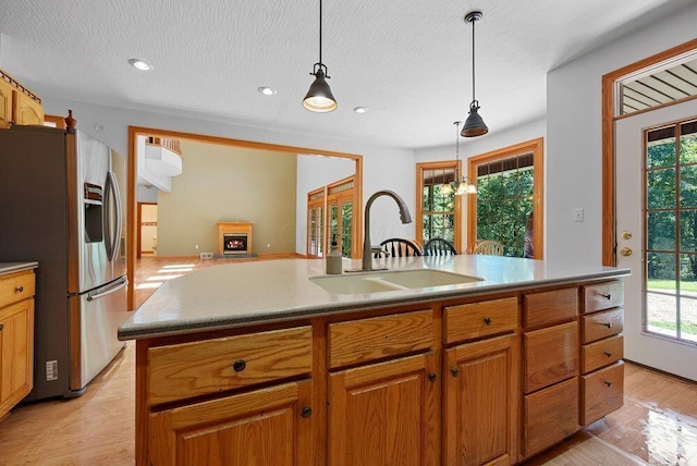 kitchen featuring a sink, light countertops, brown cabinetry, stainless steel fridge with ice dispenser, and an island with sink