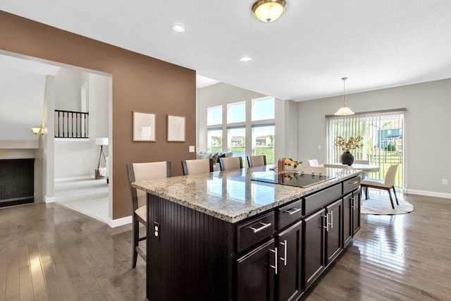 kitchen with light stone counters, black electric cooktop, a kitchen island, hanging light fixtures, and a breakfast bar area