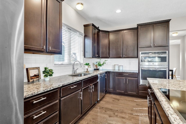 kitchen with appliances with stainless steel finishes, light wood-type flooring, tasteful backsplash, dark brown cabinets, and sink