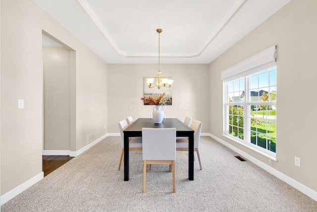 dining space with a raised ceiling, carpet floors, and an inviting chandelier