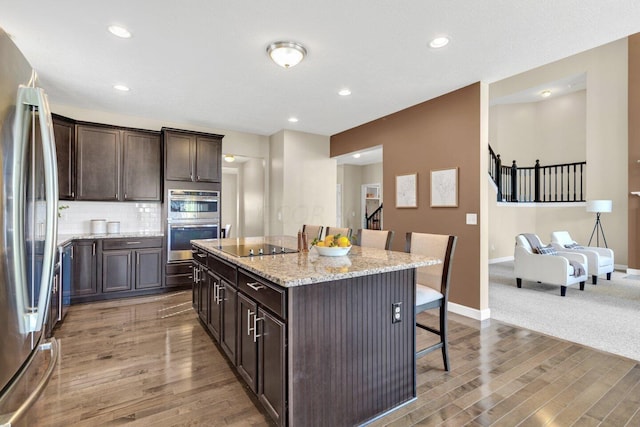 kitchen with a kitchen breakfast bar, dark hardwood / wood-style flooring, light stone counters, stainless steel appliances, and a kitchen island