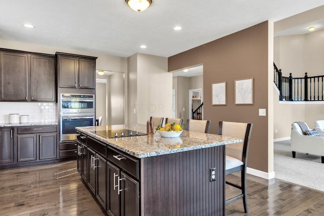 kitchen featuring a center island, a kitchen bar, black electric stovetop, dark hardwood / wood-style flooring, and stainless steel double oven