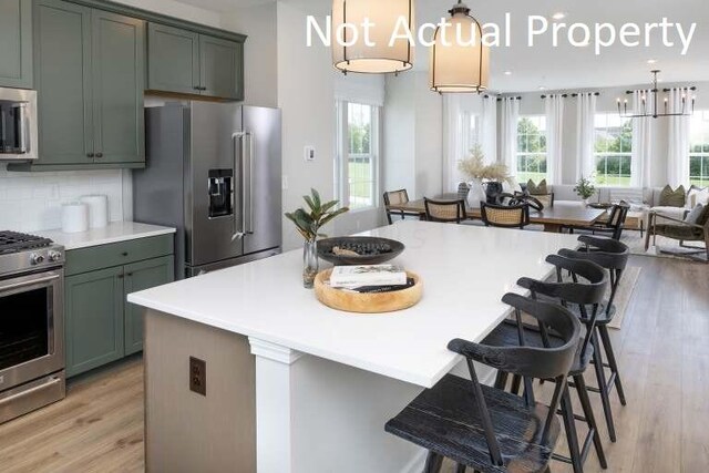 kitchen featuring a breakfast bar area, stainless steel appliances, decorative backsplash, light wood-style floors, and open floor plan