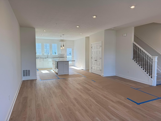 unfurnished living room with stairway, light wood-type flooring, visible vents, and recessed lighting