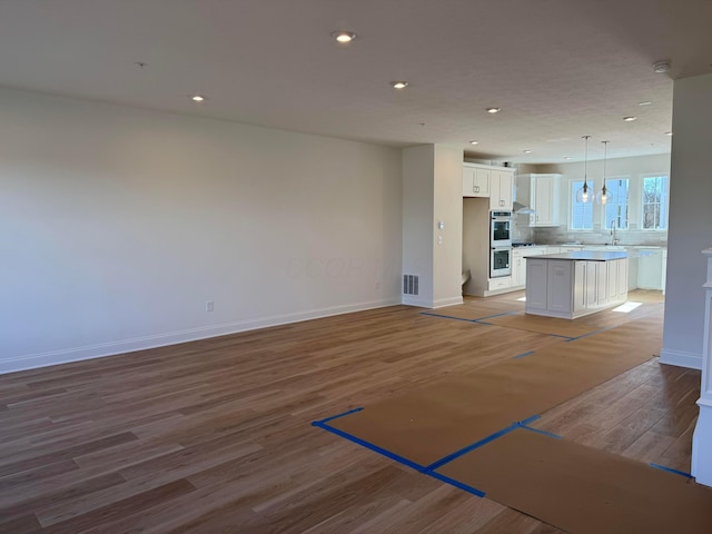 unfurnished living room with baseboards, recessed lighting, a sink, and light wood-style floors