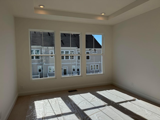 carpeted empty room with recessed lighting, a raised ceiling, visible vents, and baseboards