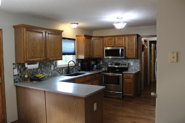 kitchen with sink, decorative backsplash, appliances with stainless steel finishes, dark hardwood / wood-style flooring, and kitchen peninsula