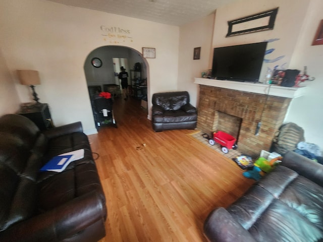 living room with a brick fireplace, a textured ceiling, and hardwood / wood-style flooring